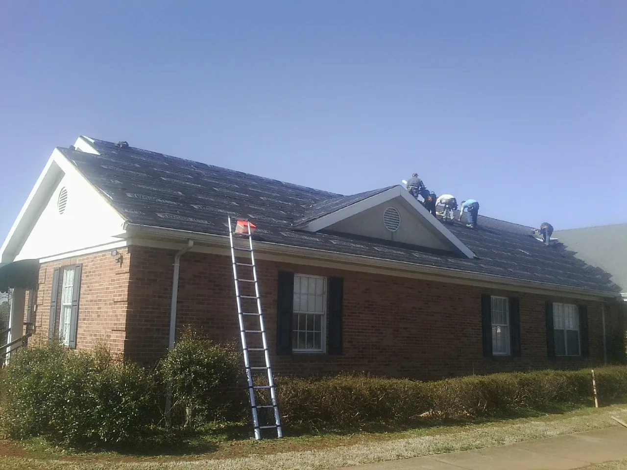 Crew tearing shingles off a brick ranch roof with a ladder set — Emergency Roof Repair work by our crew in Licking