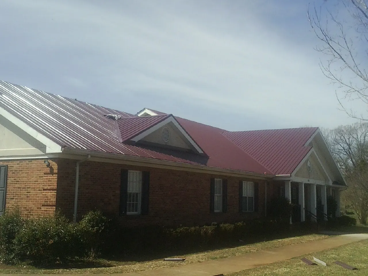Red metal roof with gabled entries on a long brick building, from a Hail Damage Roof Repair job in Licking