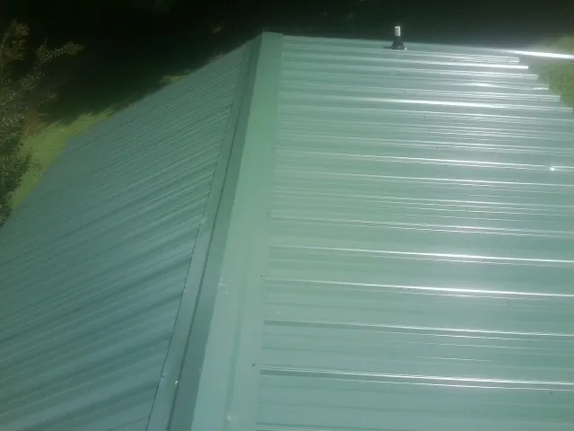 New green metal panels meeting at the ridge of a roof — Flat Roof Repair work by our crew in Licking