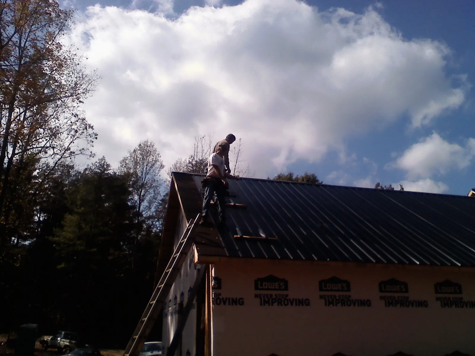 Roofer fastening dark metal panels high against a cloudy sky, from a Roof Inspection job in Licking